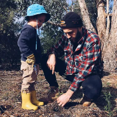 man in red white and blue plaid button up shirt with a child planting a tree.